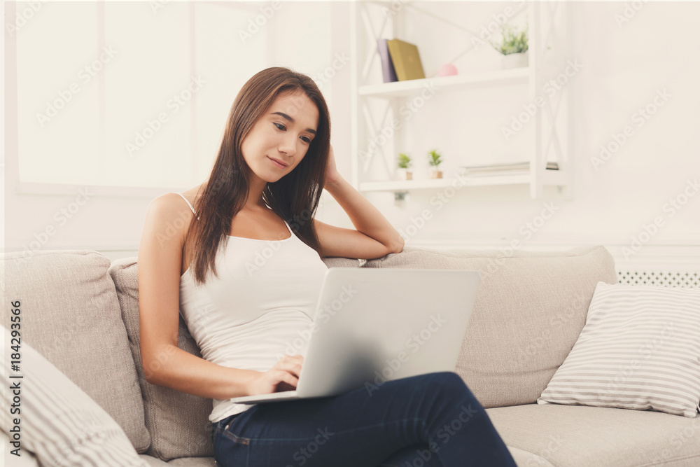 Young women using laptop sitting on sofa in white livingroom Young women using laptop sitting on sofa in white livingroom