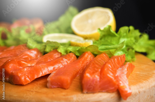 pieces of red fish with lemon and cherry tomatoes on a wooden board on a black background