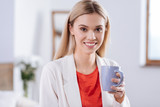 Coffee break. Charming young woman in a red blouse and a pale pink jacket holding a cup of coffee while smiling at the camera