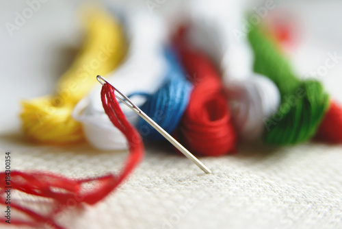 Needle in canvas with threads of different colors for embroidery. Embroidery macro close up. View from above. Free copy space.