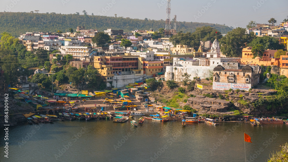 Obraz premium Omkareshwar cityscape, India, sacred hindu temple. Holy Narmada River, boats floating. Travel destination for tourists and pilgrims.