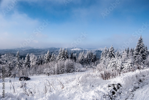 winter mountain landscape with snow covered road, forest, hills, snow and blue sky with clouds photo