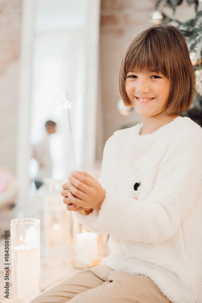 Pretty little girl in white sweater sits before a Christmas tree Pretty little girl in white sweater sits before a Christmas tree