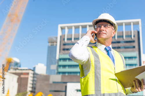 Man architector outdoor at construction area having mobile conversation photo