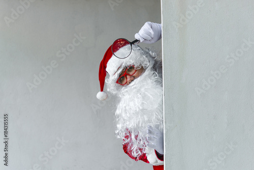 Portrait of Santa claus holding Magnifier in hand after dirty wall,Thailand people,Sent happiness for children,Merry christmas,Welcome to winter