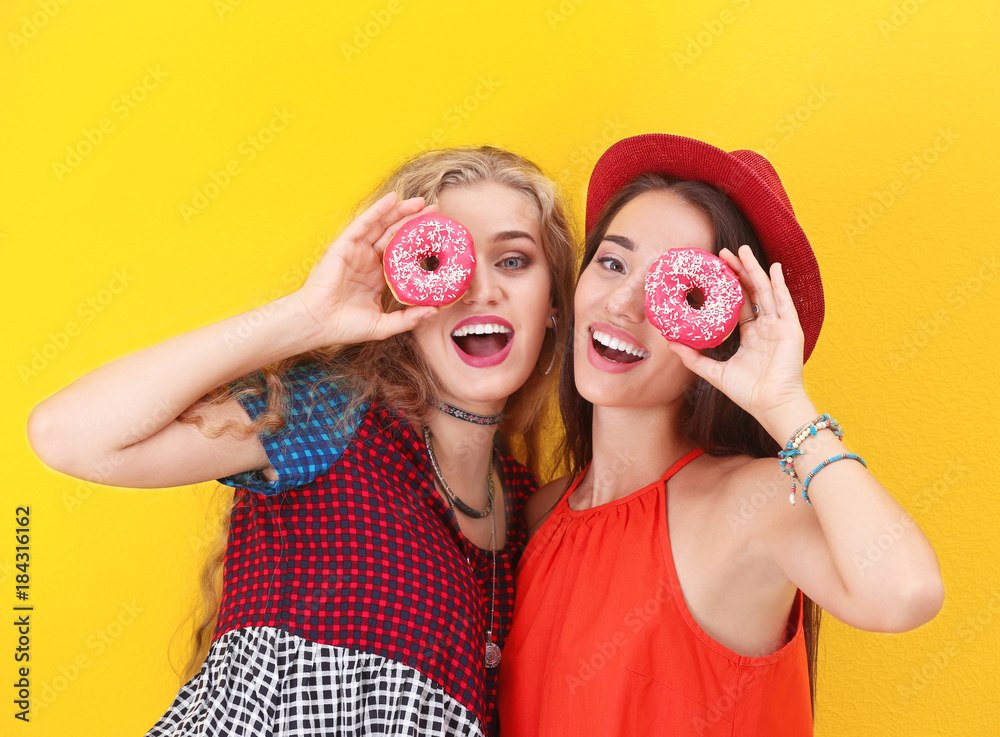 Attractive hipster girls posing with donuts on color background