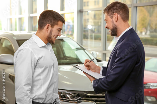 Handsome car salesman with trainee in dealership centre