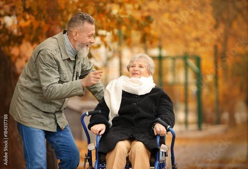 Senior man with his wife in wheelchair outdoors on autumn day