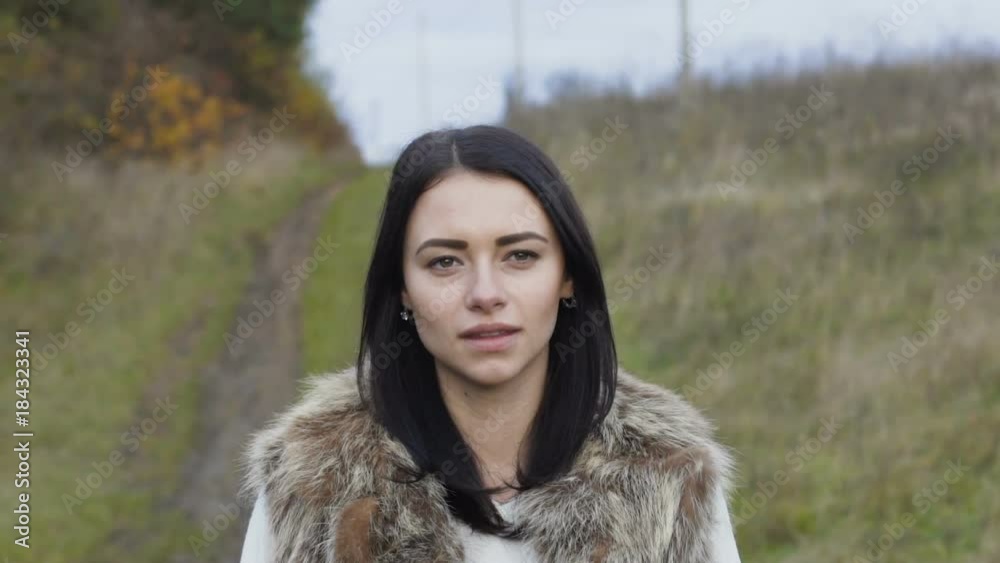 Portrait of pretty brunette walks at forest and looks at camera