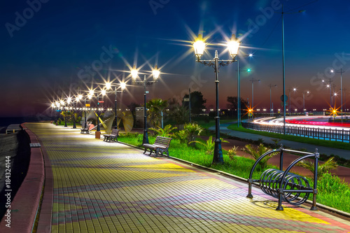 Night quay paved with sidewalk tiles, along the path are benches and lampposts. Embankment on the Black Sea coast, Sochi, Russia.