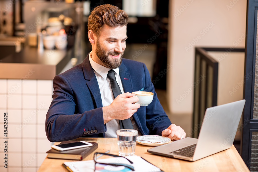 Portrait of a handsome businessman stricly dressed in the suit working with laptop at the modern cafe interior