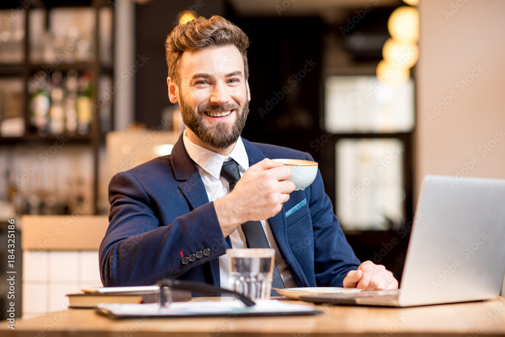 Portrait of a handsome businessman stricly dressed in the suit working with laptop at the modern cafe interior during the coffee break Portrait of a handsome businessman stricly dressed in the suit working with laptop at the modern cafe interior during the coffee break