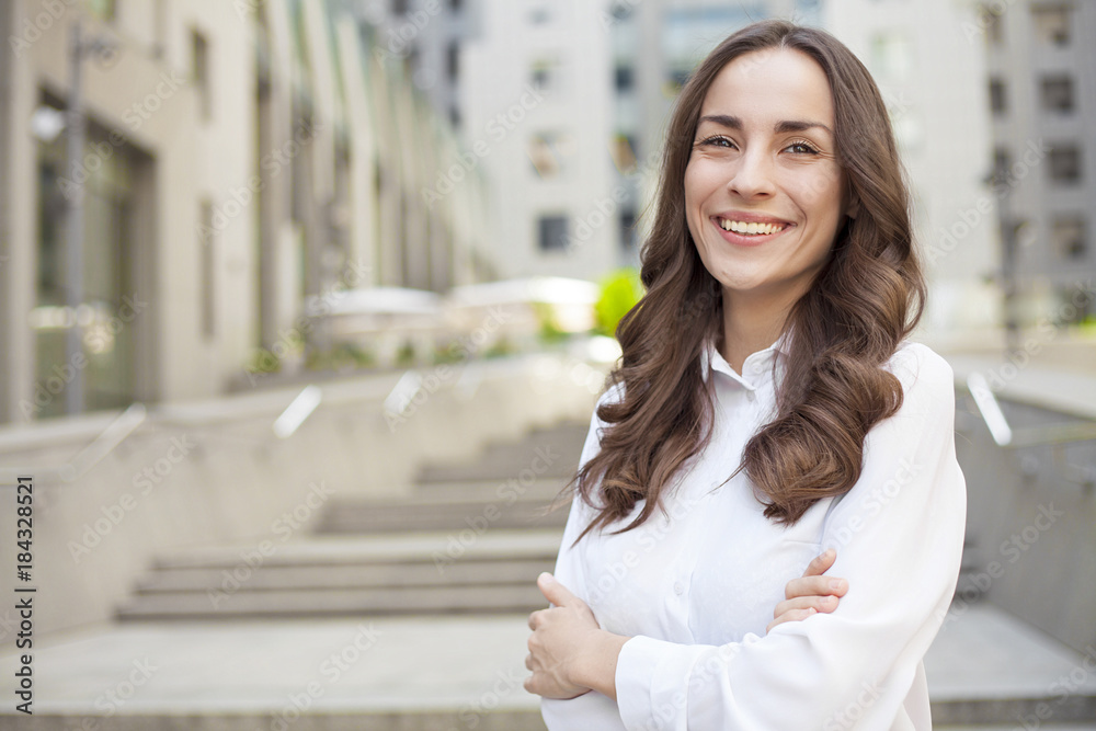 Portrait of a confident modern business woman with beautiful lush hair on the background of an office center in the city and looks on camera.