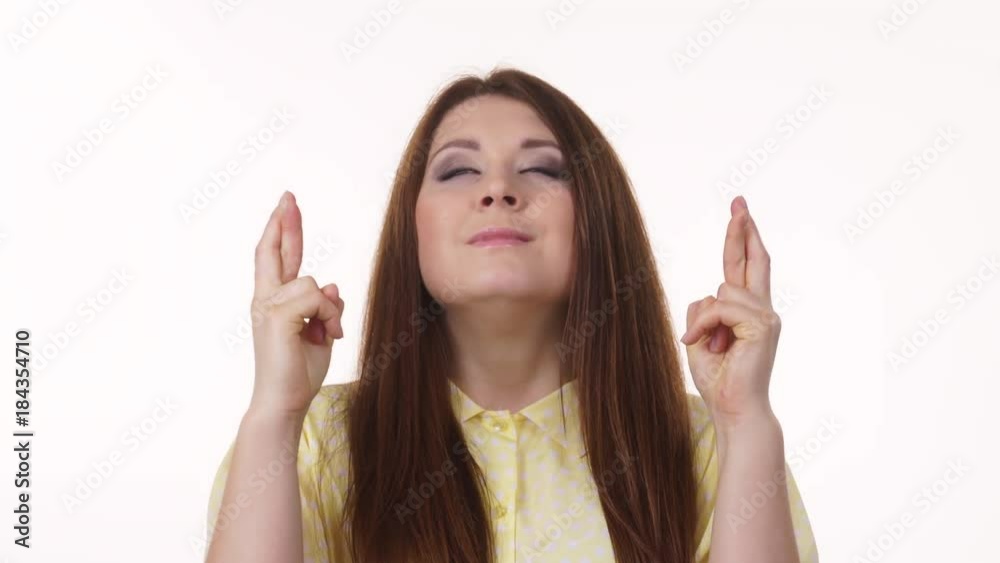 Young woman hopeful eyes closed keeping her fingers crossed hoping, asking for best, good luck, on white. Human face expressions, emotions 4K