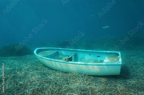 Underwater a small boat sunken on the seabed with leaves of Neptune grass and some fish, Mediterranean sea, Catalonia, Costa Brava, Spain