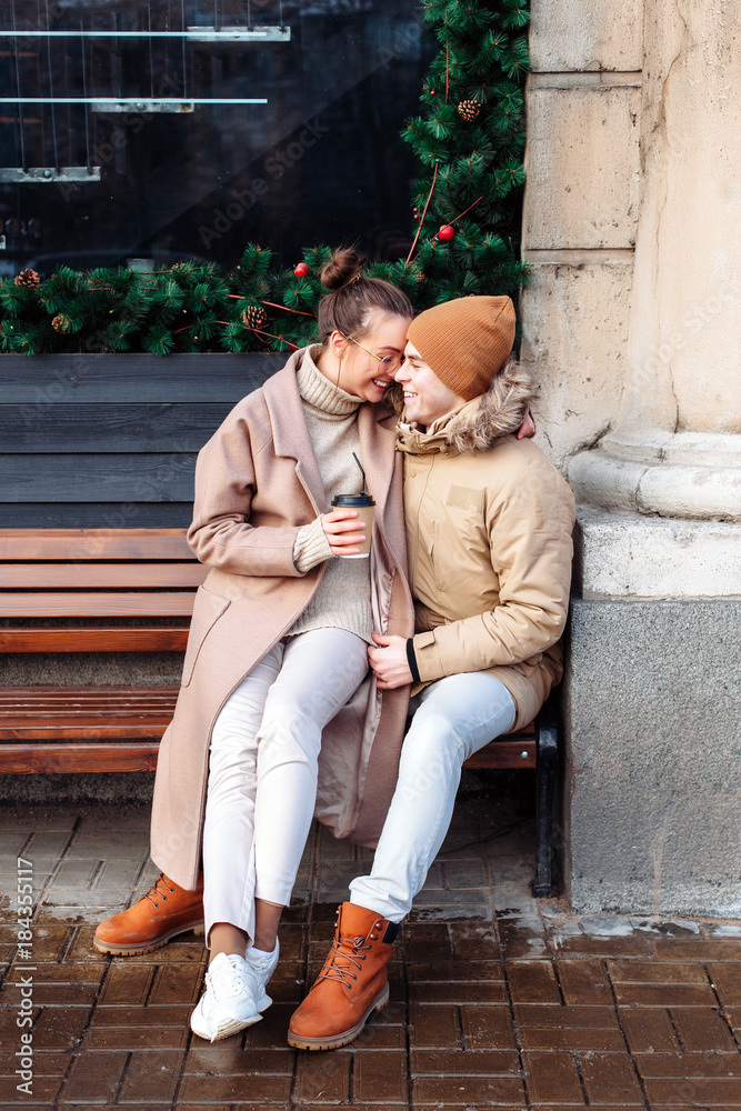 Beautiful happy young funny couple have fun together outdoor on the street in cold winter. Drinking coffee and hugging