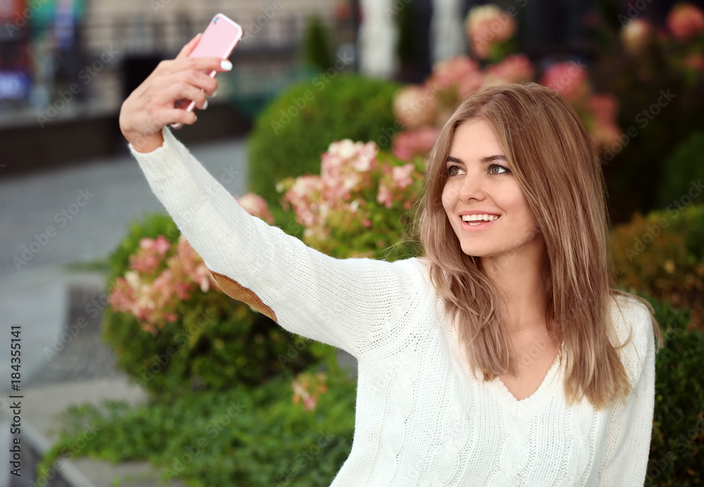 Naklejka premium Beautiful young woman taking selfie outdoors