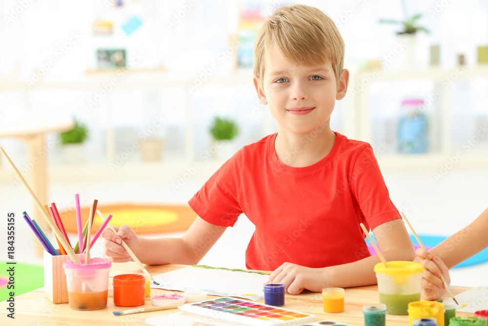 Cute boy painting picture at table indoors Cute boy painting picture at table indoors