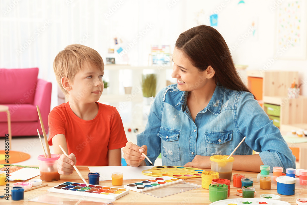 Cute boy with mother painting at table in room Cute boy with mother painting at table in room