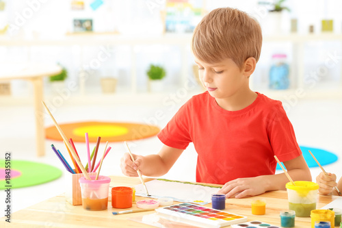 Cute boy painting picture at table indoors
