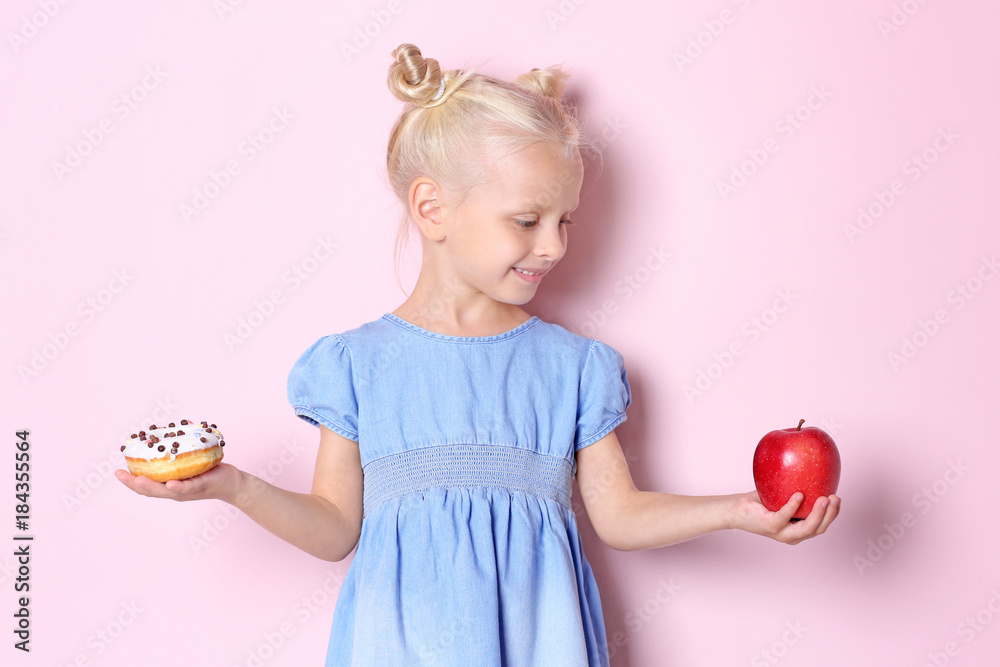 Little girl with sweet donut and fresh apple on color background Little girl with sweet donut and fresh apple on color background