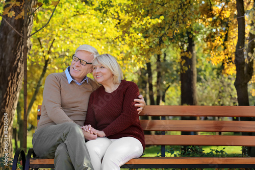 Cute elderly couple sitting on bench in autumn park