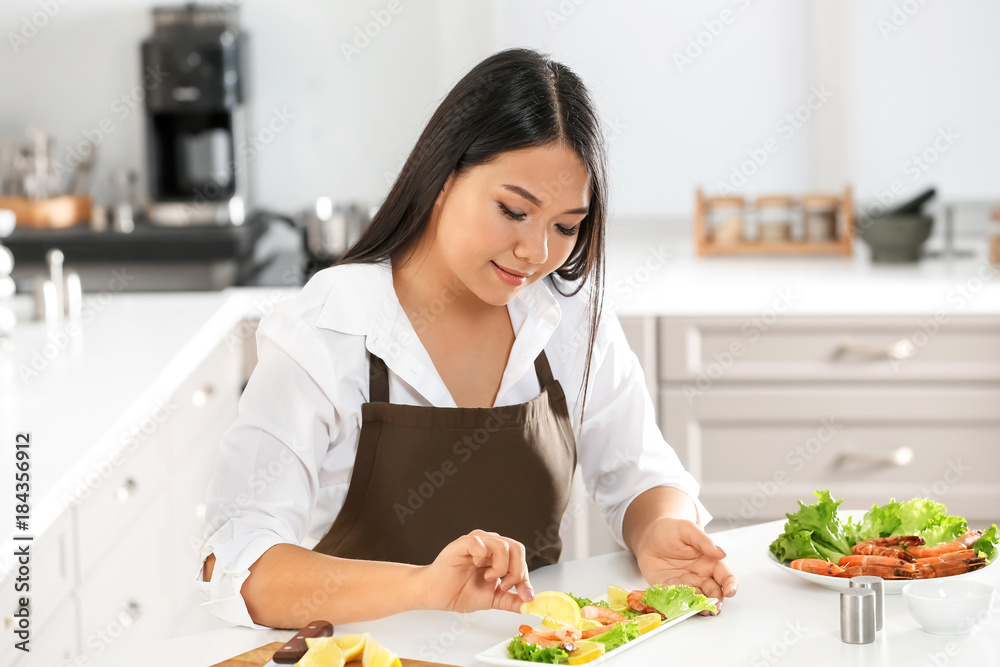 Beautiful Asian woman preparing dish with shrimps at table in kitchen