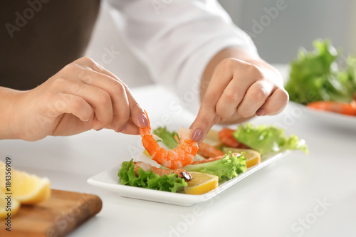 Female chef preparing dish with shrimps at table