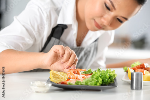 Beautiful Asian woman preparing dish with shrimps at table in kitchen