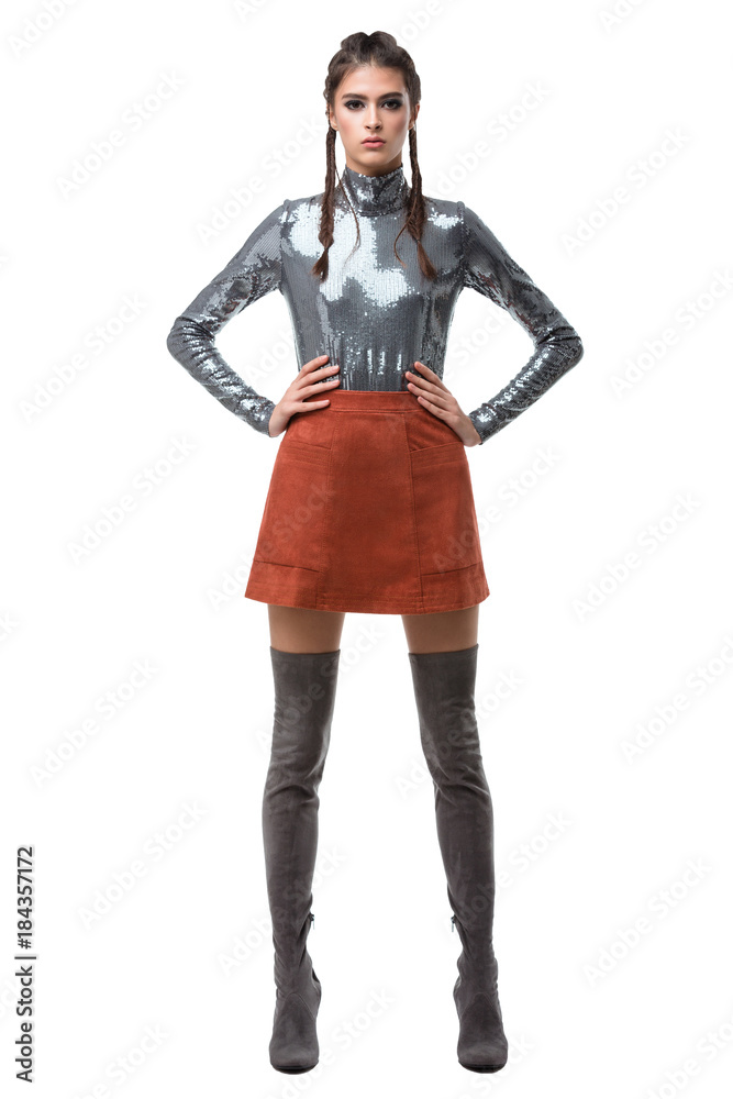 Young beautiful lady standing in light brown skirt and silver top with sequins and knee high boots on white background