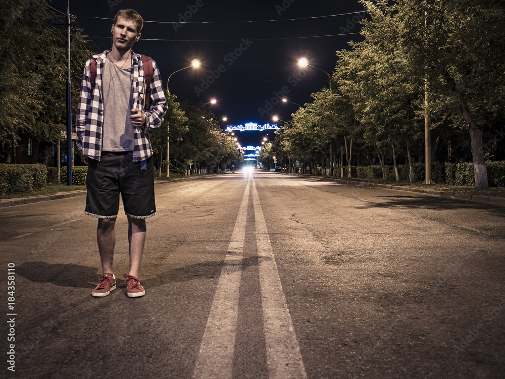 man standing on the road at night in the city looking forward, light background.