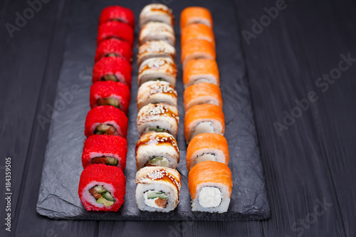 Tasty great colorful set of fresh japanese sushi maki philadelphia and california rolls served on black slate. Food art, traditional seafood, restaurant menu photo