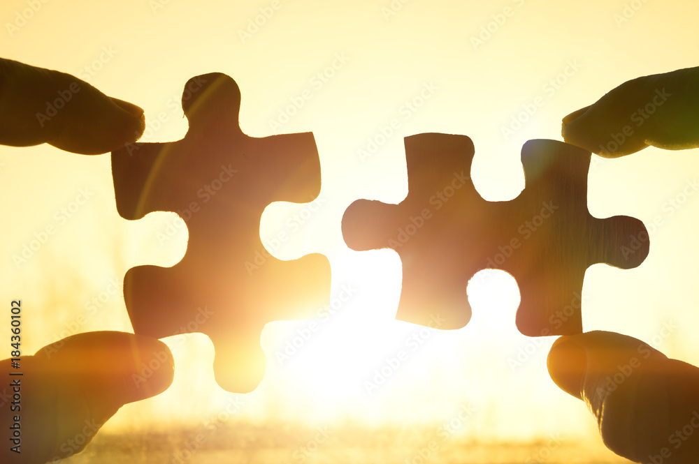 two hands trying to connect couple puzzle piece with sunset background.  Jigsaw alone wooden puzzle against sun rays. Close-up. Teamwork,  partnership, business, cooperation and management concept. Stock Photo |  Adobe Stock