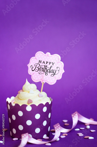 Cupcake with small decorative hearts and happy birthday sign, against violet background