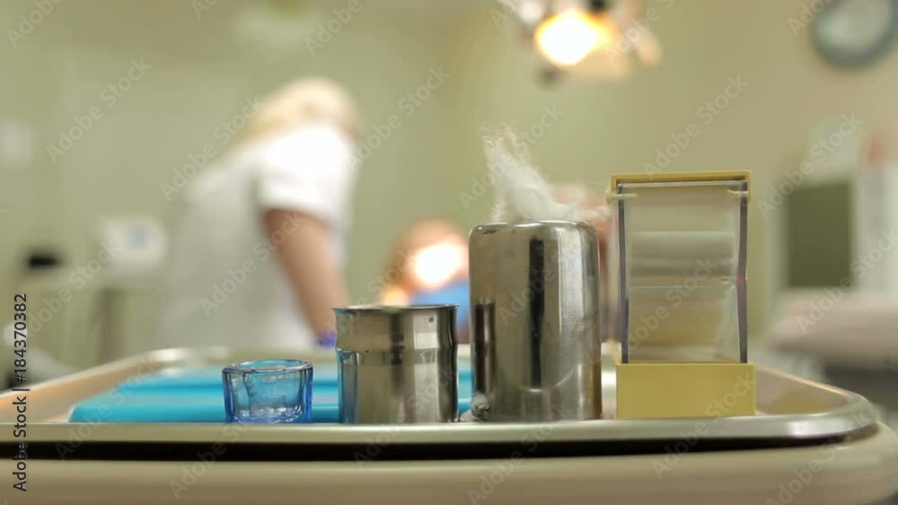 Dentist tools in metal tray on table close-up. Set of dentistry medical equipment tools on stomatology table. A set of dental instruments on the background of a silhouette of a dentist and patient. Dentist tools in metal tray on table close-up. Set of dentistry medical equipment tools on stomatology table. A set of dental instruments on the background of a silhouette of a dentist and patient.