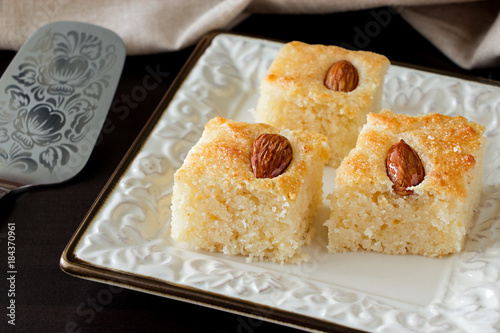 Closeup Three Pieces Basbousa Traditional Arabic Semolina Cake with Almond Nuts Orange Blossom Water. Copy space. Dark background. photo