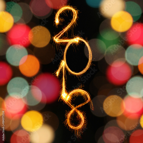 2018 vertical text align written with Sparkle fireworks and blurred unfocused bokeh gold lights on black background