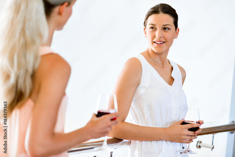 Young woman with her friend holding a glass of wine indoors Young woman with her friend holding a glass of wine indoors