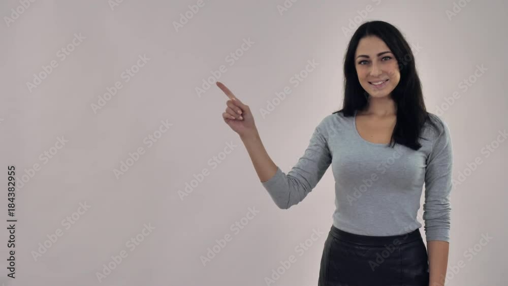 Beautiful businesswoman mixed race caucasian woman with black straight hair pointing with her finger on three items. Portrait woman wearing casual grey shirt posing in studio on background Beautiful businesswoman mixed race caucasian woman with black straight hair pointing with her finger on three items. Portrait woman wearing casual grey shirt posing in studio on background