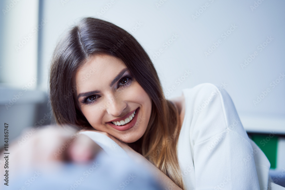 Beautiful young woman looking at camera and smiling sitting on sofa at home Beautiful young woman looking at camera and smiling sitting on sofa at home