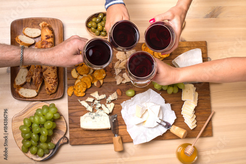 Frends eating cheese with grapes and drinking wine at home together, cheese party concept.