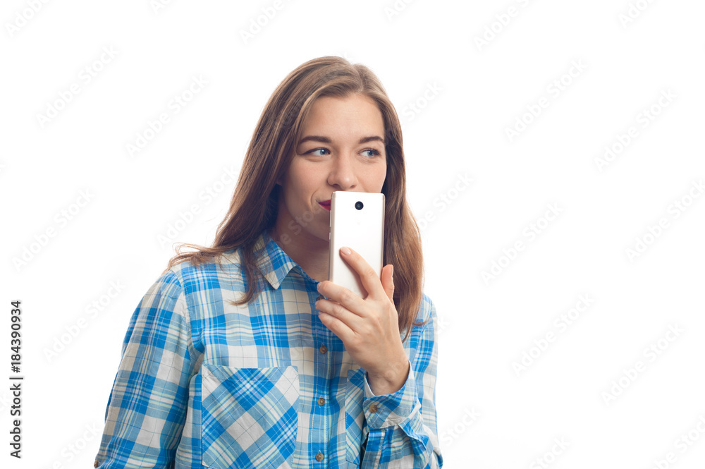 Portrait of a smiling caucasian woman in plaid shirt holding smartphone covering her mouth on a white background Portrait of a smiling caucasian woman in plaid shirt holding smartphone covering her mouth on a white background