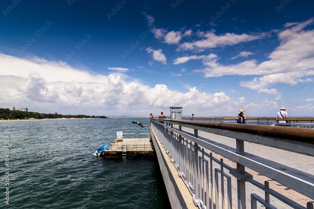 boy jumped from bridge to water. summer fun in hot weather. jump in water.. crystal clear seawater and child jumps into the water against a blue sky with beautiful white clouds.