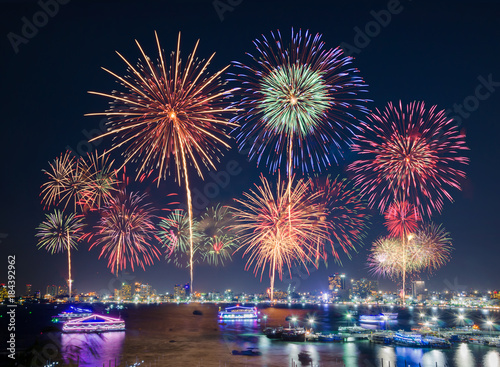 Fireworks over cityscape by the beach and sea surrounding with hotels, restaurant, and service boats and cruises during blue twilight time for celebrating New Year eve and special occasion on holidays