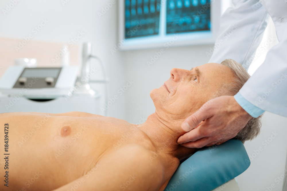 Medical therapy. Nice pleasant serious man lying on the massage bed and looking up while undergoing physiological therapy