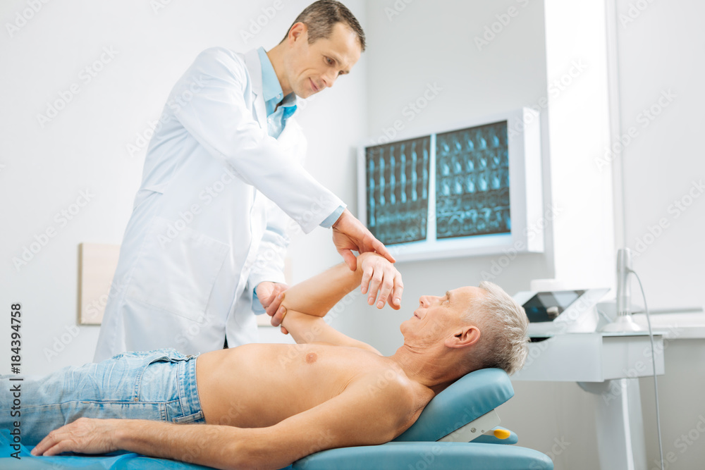 Obraz premium At the hospital. Nice serious male doctor standing near his patient and doing a medical checkup while working in the hospital