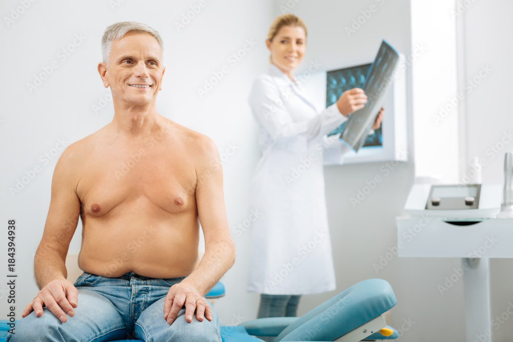 Optimistic attitude. Joyful delighted senior man sitting on the medical bed and smiling while being in the positive mood Optimistic attitude. Joyful delighted senior man sitting on the medical bed and smiling while being in the positive mood