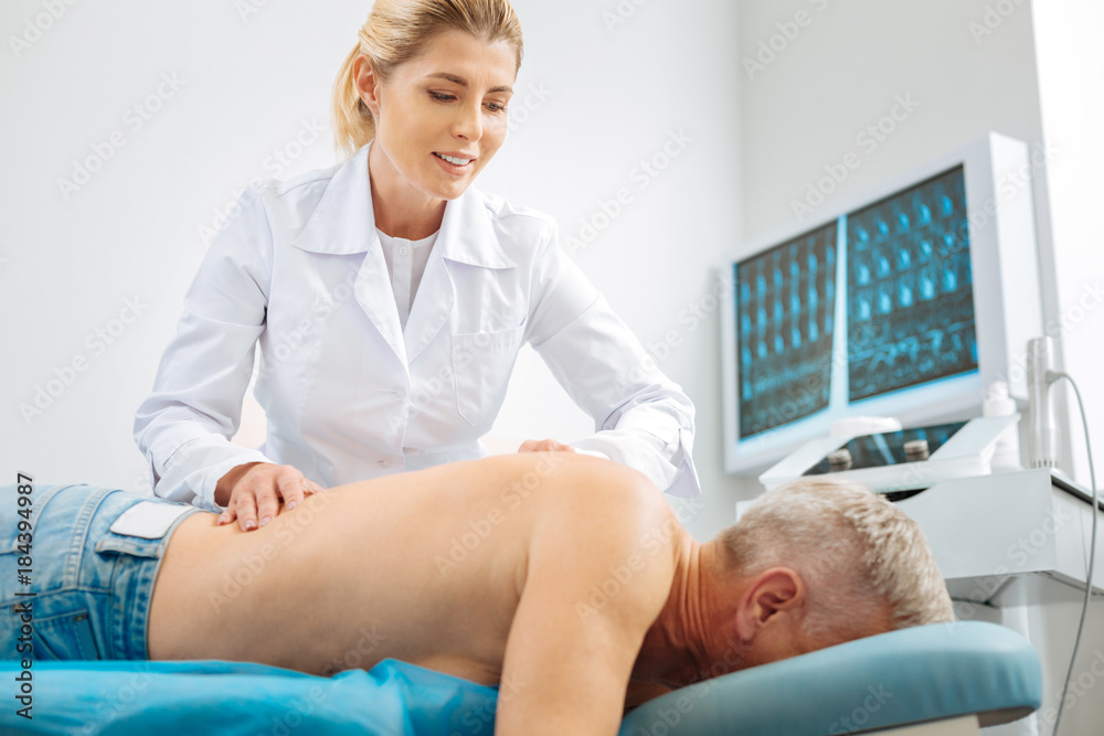 Obraz premium Medical therapy. Professional delighted female doctor smiling and doing a massage while working with her patient