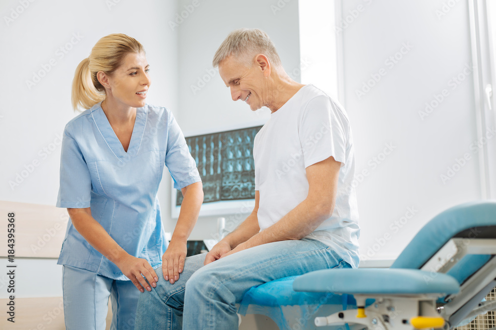 Medical care. Delighted nice female doctor looking at her patient and doing physiotherapy while working in the hospital Medical care. Delighted nice female doctor looking at her patient and doing physiotherapy while working in the hospital