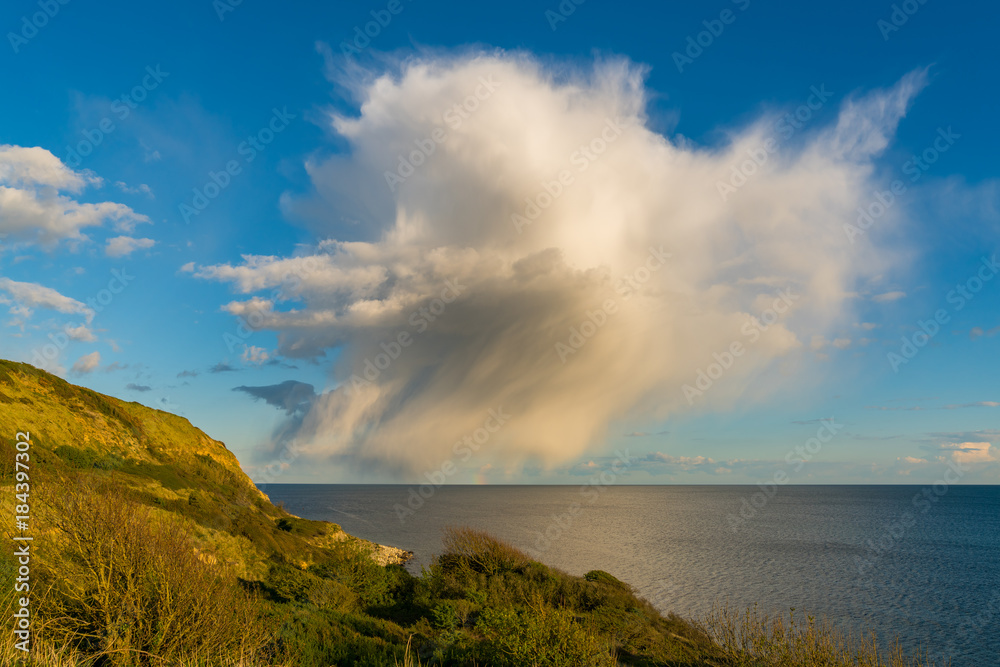 Single Raincloud with a little bit of a rainbow at Osmington Bay, near Weymouth, Jurassic Coast, Dorset, UK